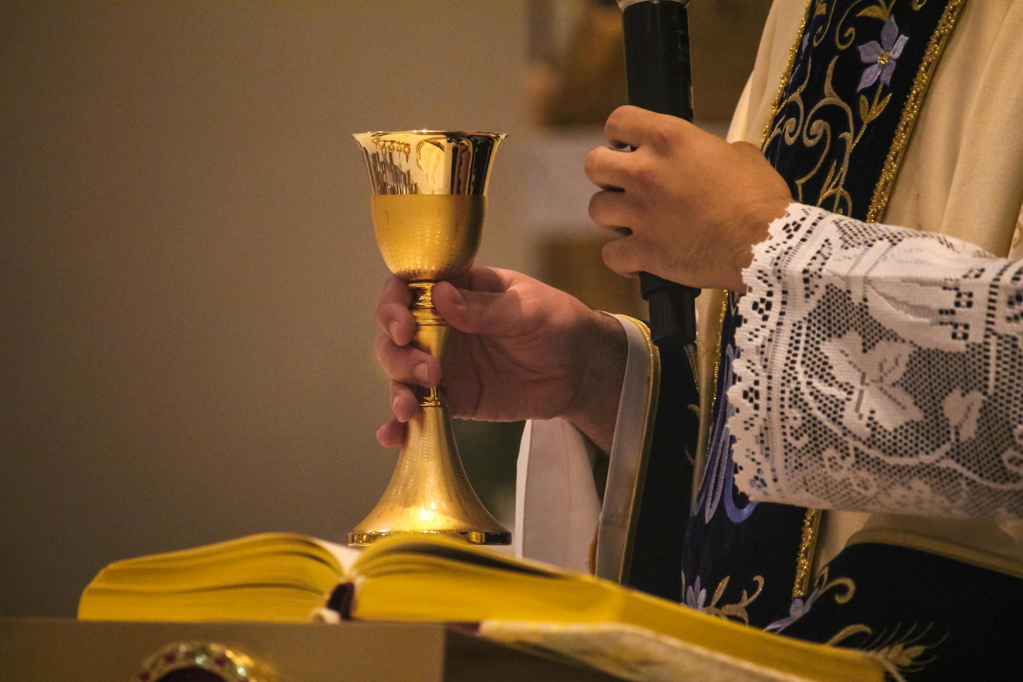Close-up of a priest holding a gold chalice during a Catholic mass ceremony.